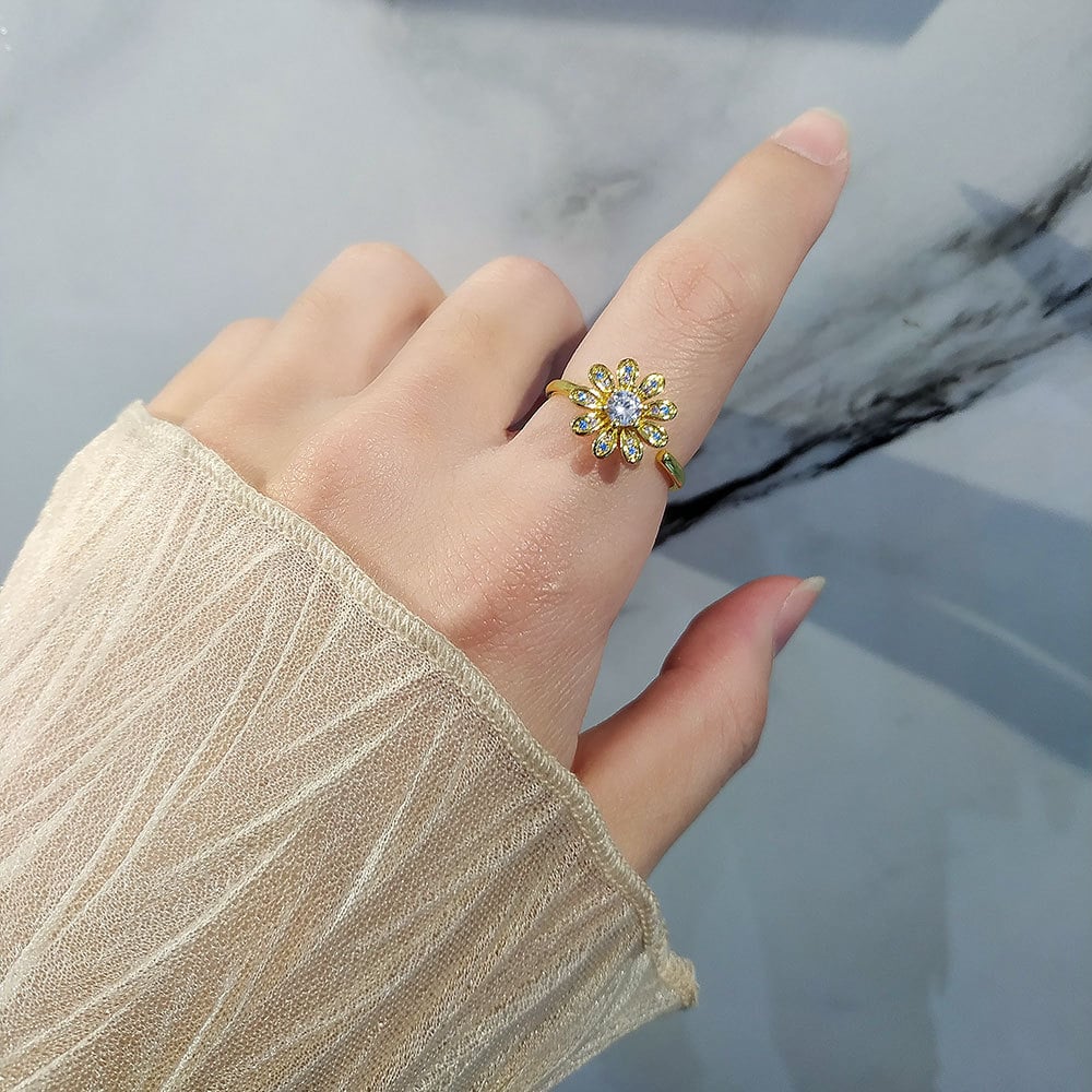 Bague anti-stress rotative Oxalis dorée, fleur aux pétales piqués de pierres bleues et roses, portée au doigt